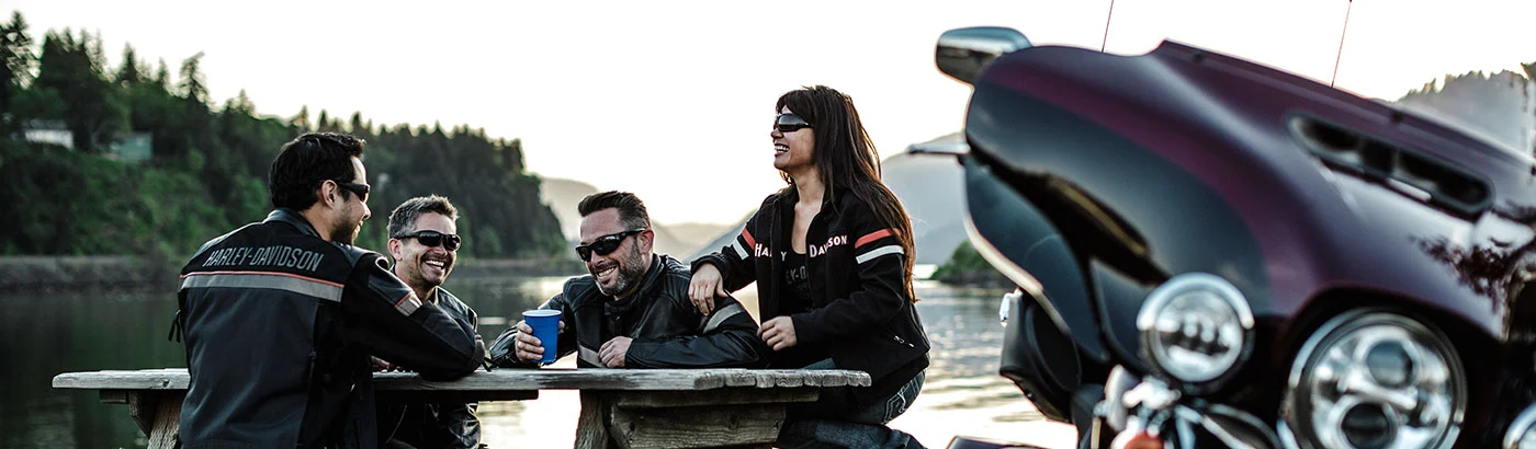 Group of motorcycle riders sitting around a picnic table next to a Harley Davidson motorcycle